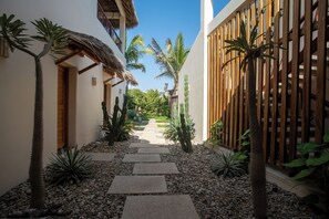 A narrow pathway with stepping stones leading to a wooden gate, surrounded by various plants and a clear blue sky.
