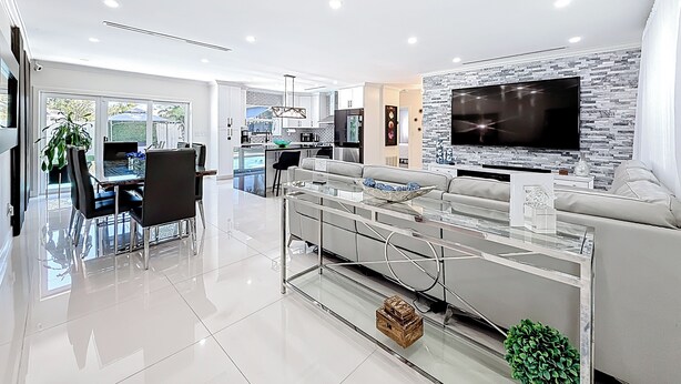 A modern living room with a large flat-screen TV mounted on a stone-textured wall, a glass coffee table, and a seating area with a sofa and chairs. - 4 bath & 4 bedroom house in beautiful Pompano Beach with AC (Pompano Beach)