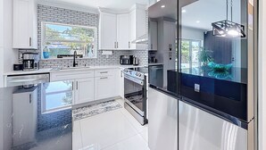 A modern kitchen with white cabinets, a black refrigerator, and a large window. - 4 bath & 4 bedroom house in beautiful Pompano Beach with AC (Pompano Beach)