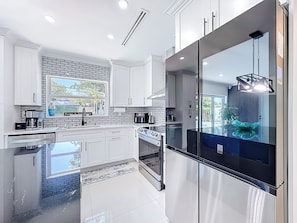 A modern kitchen with white cabinets, a black refrigerator, and a large window. - 4 bath & 4 bedroom house in beautiful Pompano Beach with AC (Pompano Beach)