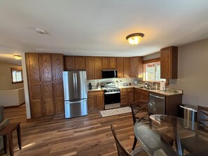 A modern kitchen with wooden cabinets, stainless steel appliances, and a glass dining table.