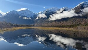 Ein ruhiger See, der schneebedeckte Berge spiegelt, umgeben von einem bewaldeten Gebiet.