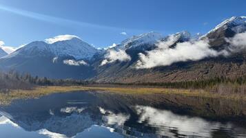 A tranquil lake reflecting snow-capped mountains, surrounded by a forested area.