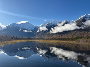 Ein ruhiger See, der schneebedeckte Berge spiegelt, umgeben von einem bewaldeten Gebiet.