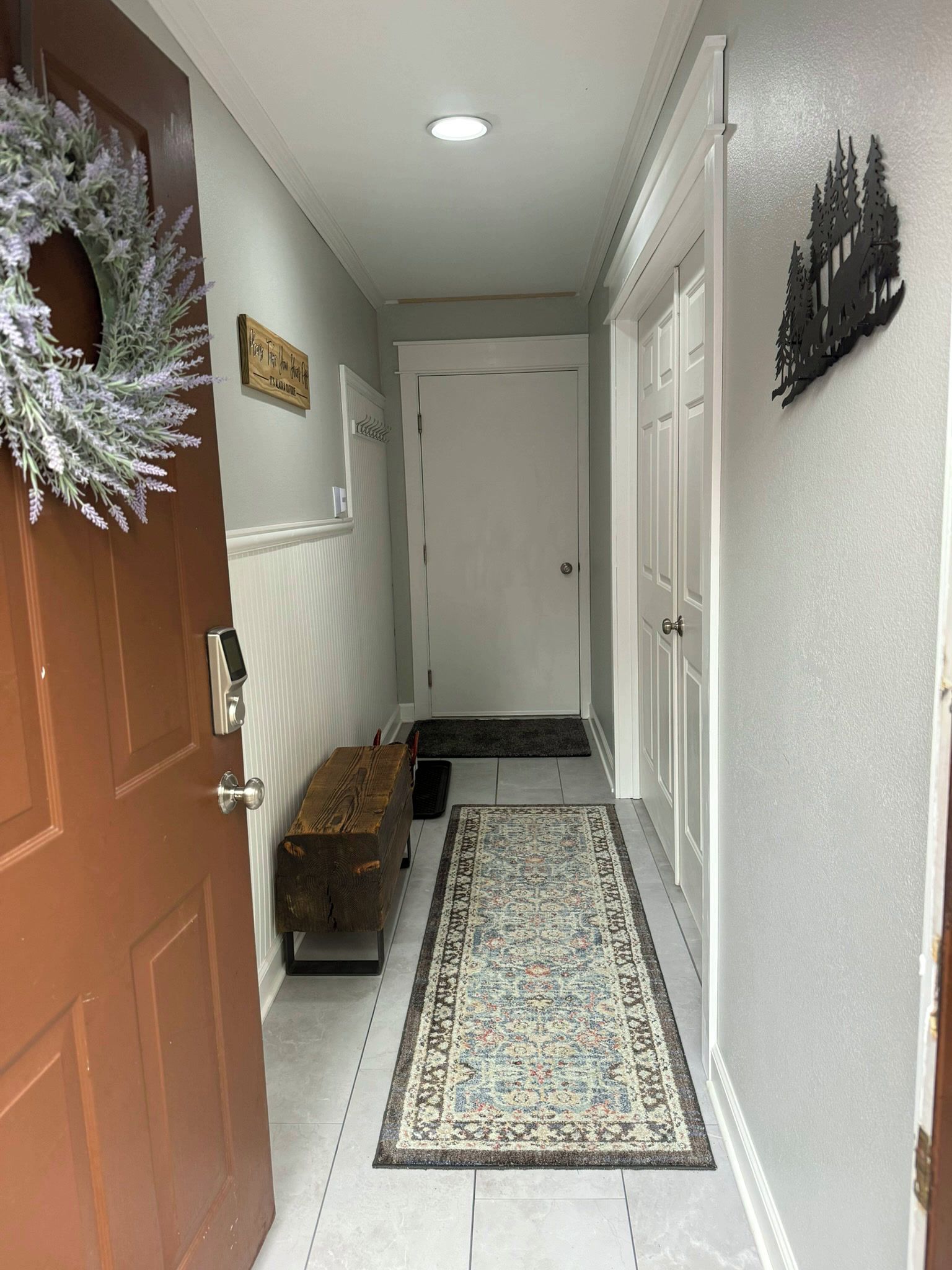 A hallway with a wooden bench, a rug, a door with a wreath, and a wall-mounted sign.