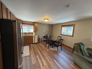 A compact kitchen with wooden cabinets, a refrigerator, a dishwasher, and a dining table with chairs.
