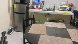 Une cuisine compacte équipée d’un réfrigérateur, d’un four à micro-ondes et d’un petit plan de travail avec un évier. On y trouve également une table à manger avec un set de table et des chaises.