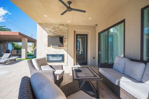 Un patio al aire libre con mobiliario de mimbre, un televisor de pantalla plana y una chimenea de piedra.