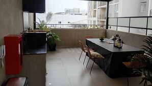 Een balkon met een tafel en stoelen, een rode kast en een aan de muur bevestigde televisie.
