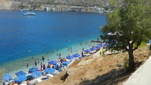 Une plage à l’eau d’un bleu cristallin, où l’on peut se baigner et bronzer, avec une chaîne de montagnes en toile de fond.