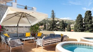 Une terrasse extérieure avec un ensemble de meubles de salon, un parasol blanc et un jacuzzi.