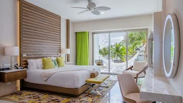 Una habitación de hotel moderna con una cama, un escritorio, una silla, un ventilador de techo y un amplio ventanal con vistas a palmeras.