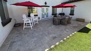 A patio with two white chairs, a table, and two red umbrellas.
