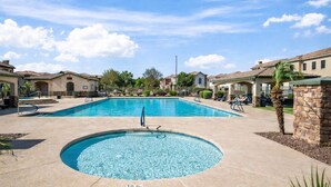 A swimming pool with a hot tub, surrounded by houses and a clear sky.