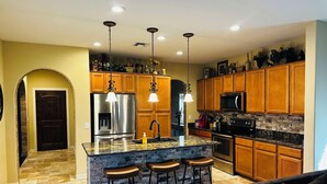 A modern kitchen with granite countertops, stainless steel appliances, wooden cabinets, and a central island with bar stools.