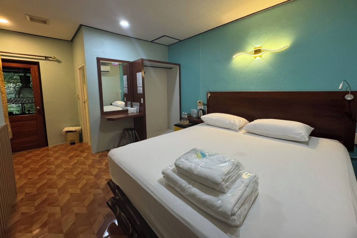 Habitación de hotel con cama, mesita de noche, espejo, puerta y lámpara de pared.