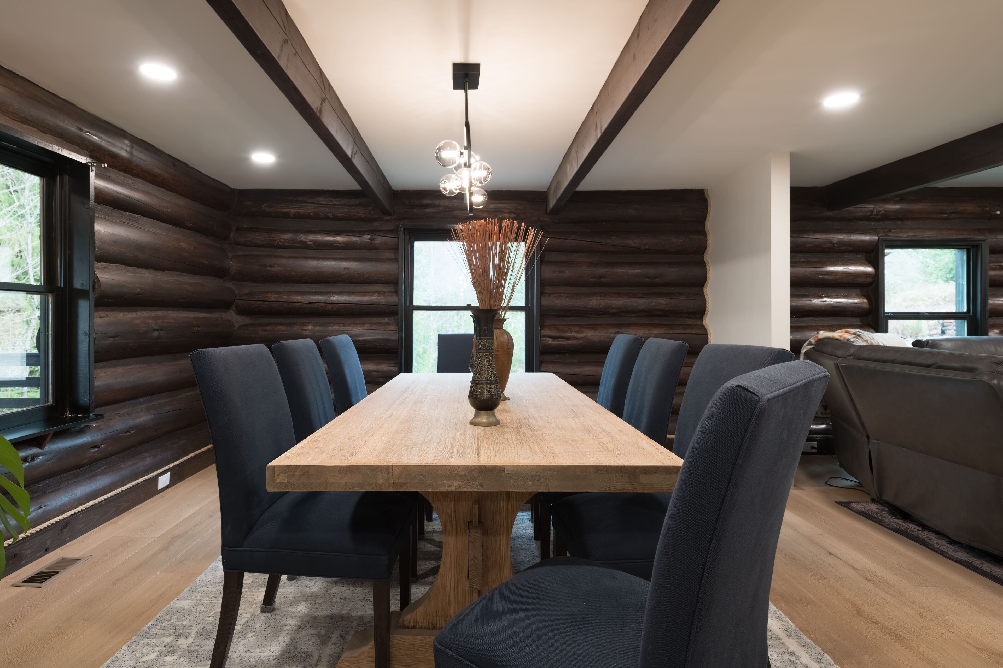 A dining area with a wooden table and chairs, a vase with dried plants, and a ceiling light fixture.
