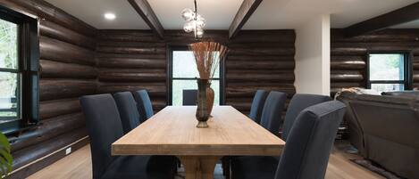 A dining area with a wooden table and chairs, a vase with dried plants, and a ceiling light fixture.