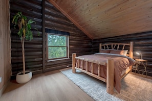 A log cabin bedroom with a wooden bed, a large window, and a potted plant.