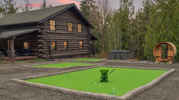 Una cabaña de troncos con un pequeño campo de práctica de golf y un barril de madera.