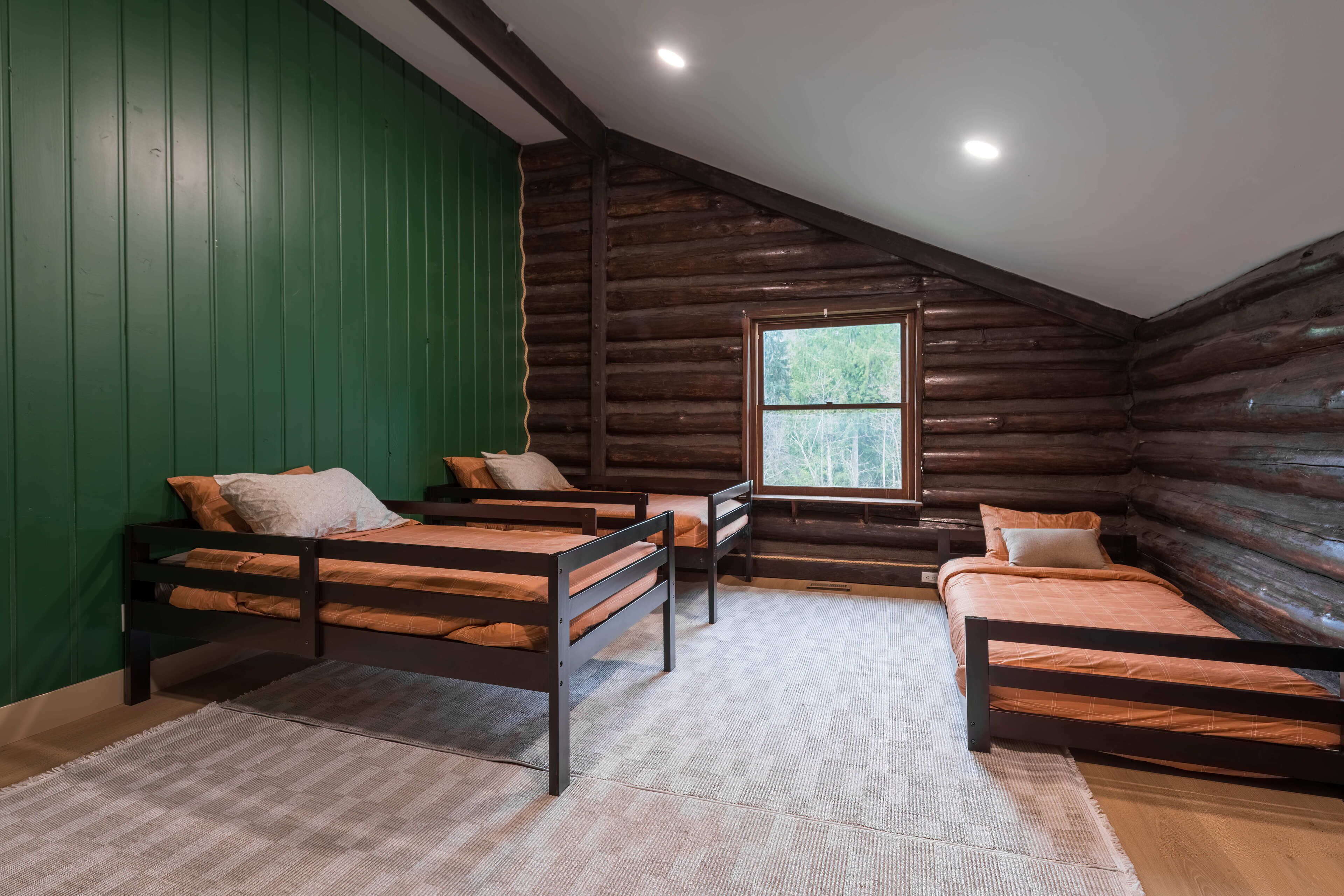 Quarto de cabana de tronco com três beliches, uma janela grande e paredes verdes.