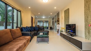 A modern living room with a brown leather sofa, a glass coffee table, and a flat-screen TV on a white console. - First Private Pool Villa, 4-bedroom private pool villa in peaceful Ao Nang, (Ao Nang)