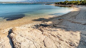 Un littoral rocheux, avec une eau claire et des montagnes qui se dessinent à l'horizon.