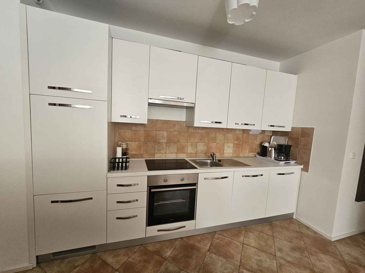 A modern kitchen with white cabinets, a stainless steel sink, and a built-in oven.