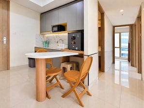 A modern kitchen with a white countertop, two wicker chairs, a GEA refrigerator, and a microwave. - Snoopy By SanLiving - 3BR - Direct Mall (Jakarta)