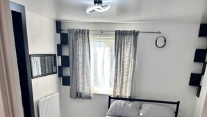 A bedroom with a bed, curtains, a radiator, and a window. - Freshly Renovated 2 bed Near City Airport (London)