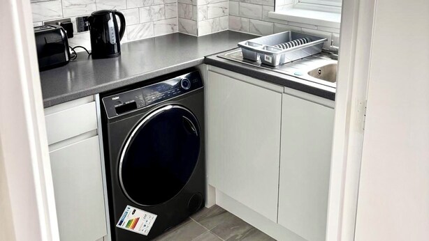 A compact kitchen with a washing machine, a coffee maker, and a toaster. - Freshly Renovated 2 bed Near City Airport (London)