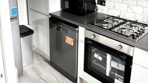 A compact kitchen with a built-in dishwasher, a microwave, a gas stove, and a stainless steel refrigerator. - Freshly Renovated 2 bed Near City Airport (London)
