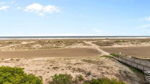 A beach with a wooden boardwalk leading to the water, sandy dunes, and a clear sky.