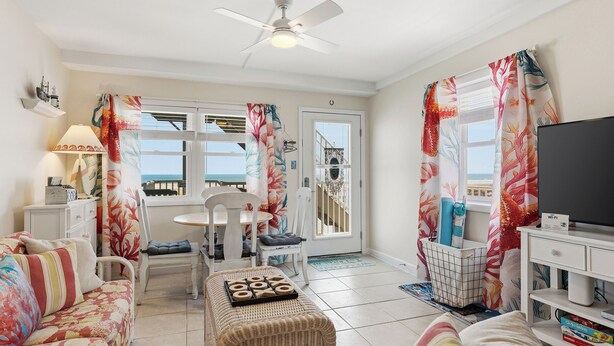 A living room with a sofa, a dining table with chairs, a TV, and a balcony with curtains.