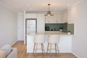 A modern kitchen with white cabinetry, a herringbone backsplash, and a central island with bar stools. - Mountain Views & Pool | 2BR Peaceful Kelvin Grove (Brisbane)