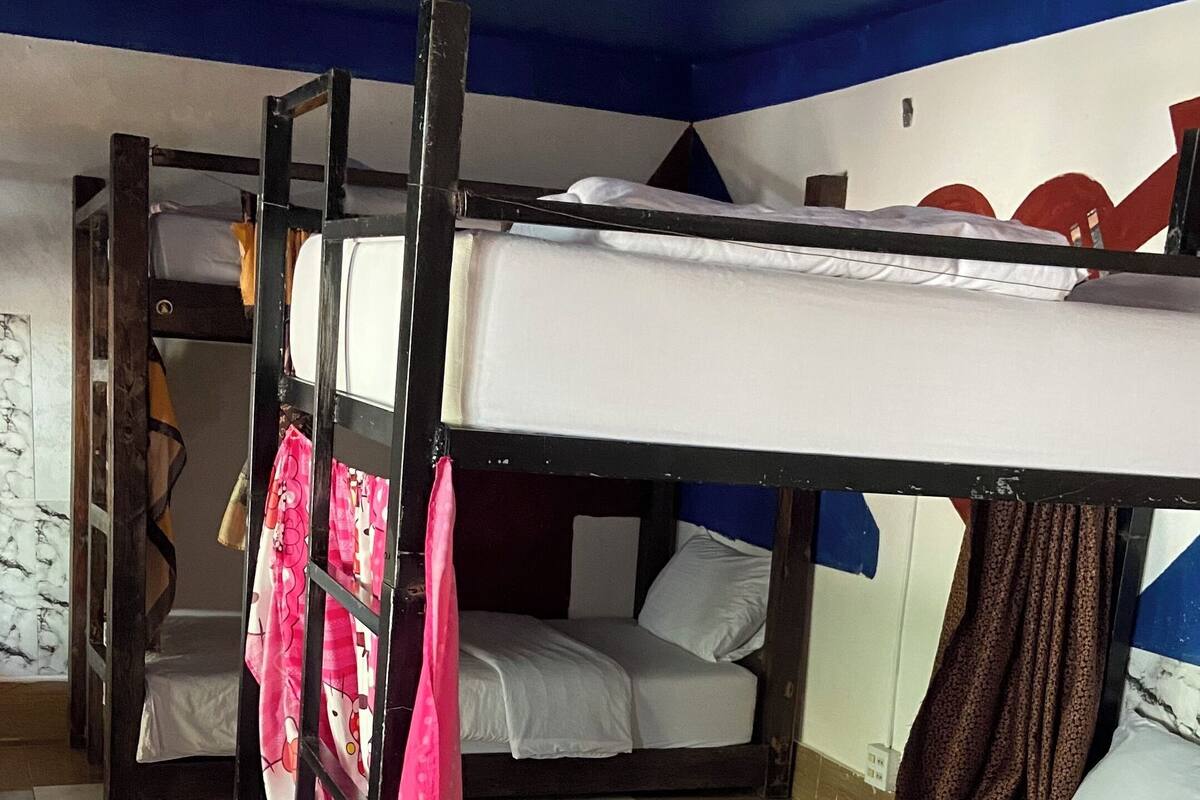 Un dormitorio con literas, piso a cuadros, techo azul y una pared con un diseño geométrico.