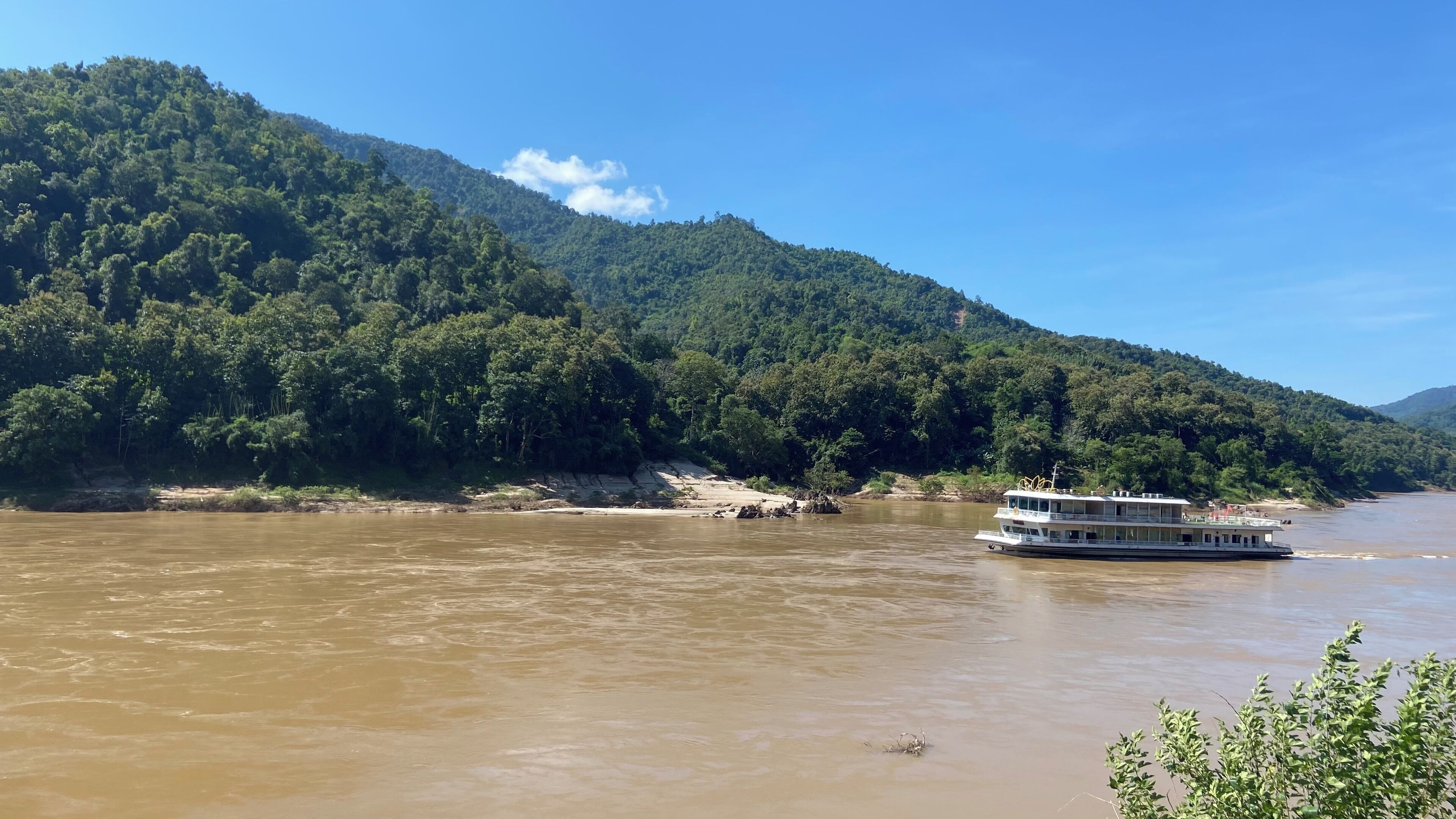 A river with a boat and a forested hillside in the background.