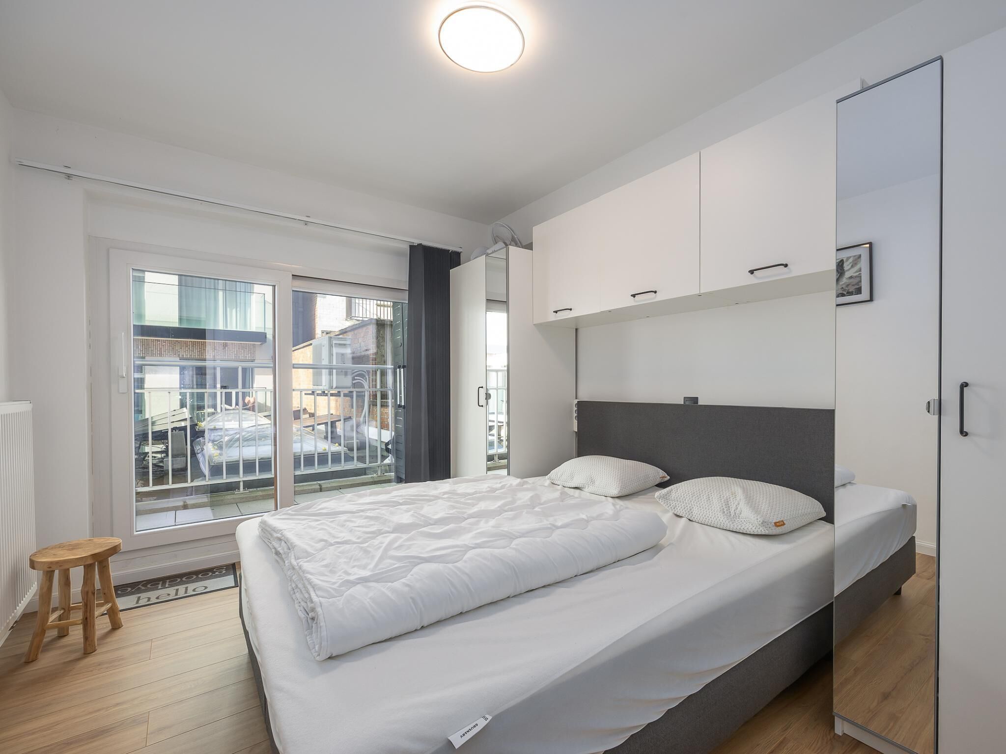 Ein modernes Schlafzimmer mit einem großen Bett, einem Kleiderschrank und Blick durch eine Glastür.