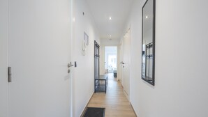 A narrow hallway with white walls, a wooden floor, and a door at the end. - Stylish apartment with terrace close to the sea (Middelkerke)
