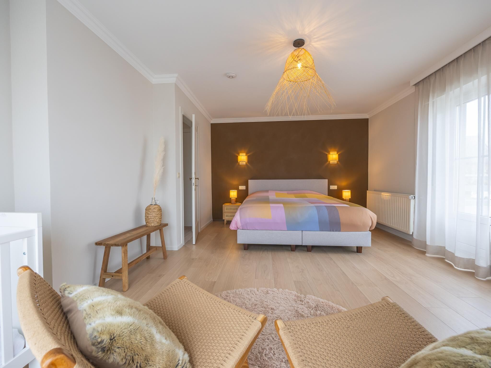 A bedroom with a bed, bedside lamps, a hanging light fixture, a wooden bench, and a fluffy rug.