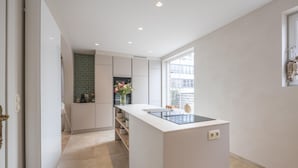 A modern kitchen with a central island, a brick backsplash, and a view through the window. - Luxury holiday home for 8 people near the sea (Westende)