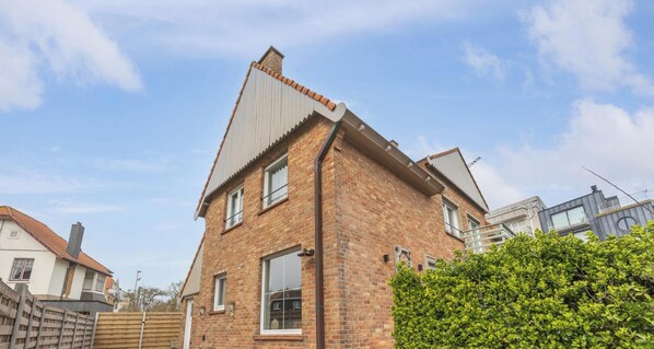 A two-story brick house with a gabled roof, multiple windows, and a wooden fence in the foreground. - Luxury holiday home for 8 people near the sea (Westende)
