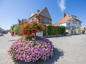 Een woonstraat met huizen, een bloembed met roze en rode bloemen, en geparkeerde auto's.