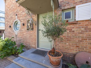 A brick building with a green door, a potted tree, and a small window. - Luxury holiday home for 8 people near the sea (Westende)