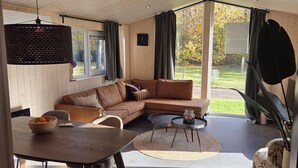 Ein modernes Wohnzimmer mit Holzausstattung, einer Couch, einem Esstisch und Blick ins Freie.