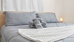 Ein ordentlich bezogenes Bett mit grauer Bettwäsche, einer weißen Tagesdecke und gefalteten Handtüchern seitlich.