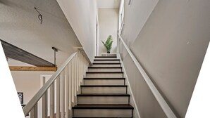 Eine Treppe mit Holzbalkendecke, weißen Wänden und einer Topfpflanze am oberen Ende.