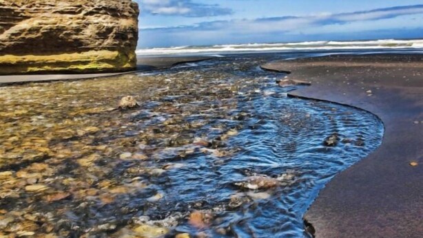 A rocky shoreline with clear water and a large rock formation. - Family Home Away From Home (Waverley)