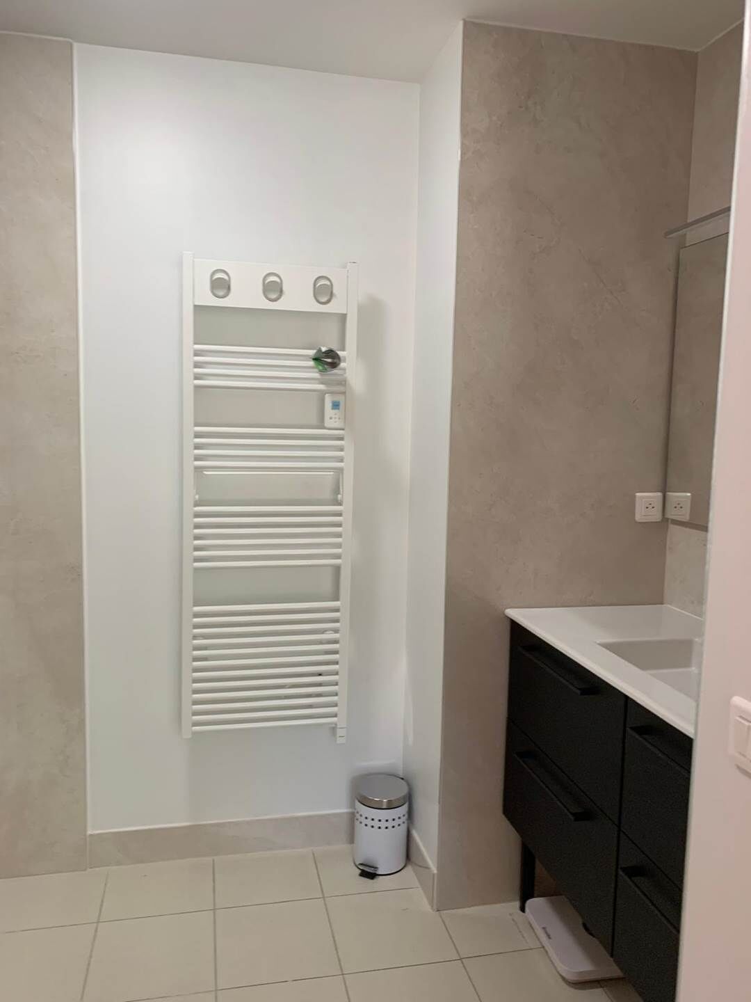 A bathroom with a white towel rack, a trash bin, and a dark-colored cabinet.