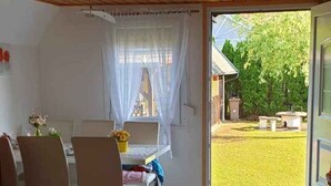 A dining area with a wooden table and chairs, a window with curtains, and a view of a yard.